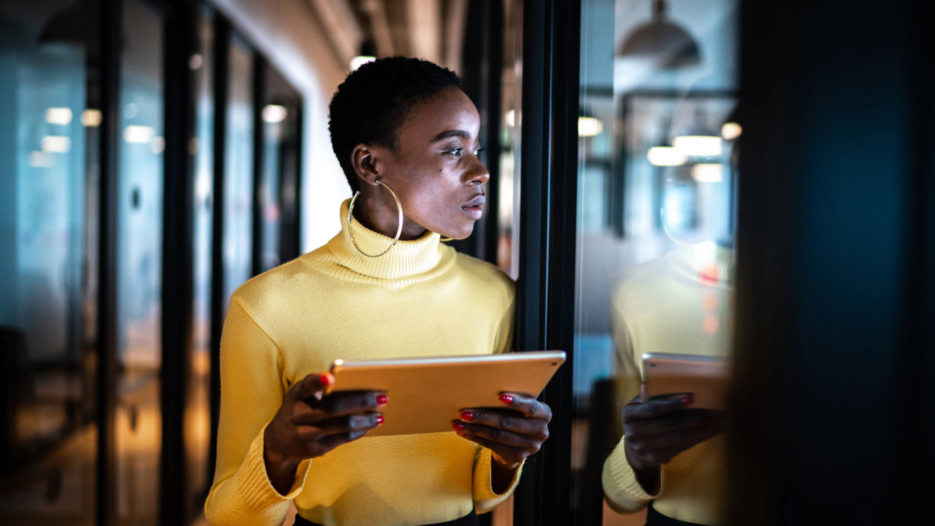 A young female sales exec standing with a tablet, representing a leader who analyzes the team’s needs before hiring rather than rushing the process.