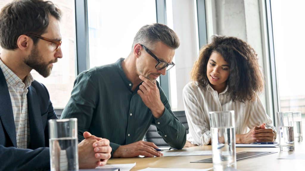 Team collaborating on business strategy with sales charts and competitive analysis presentation in a modern office setting.