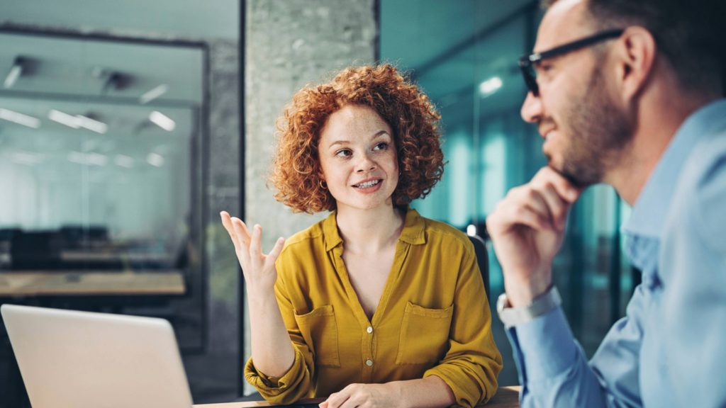 Smiling woman in a yellow blouse leading a conversation with a colleague during a business meeting.